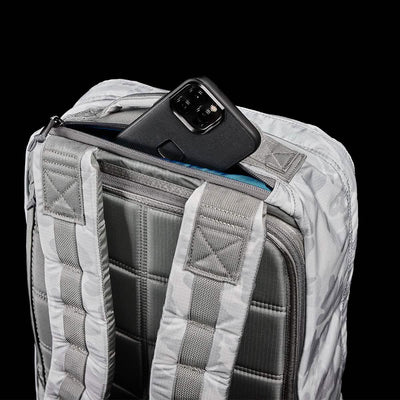 A GR1 USA - Ripstop ROBIC® rucksack by GORUCK in gray, showcasing its ultra-lightweight design with padded straps and a quilted back panel, is partially open to reveal a black smartphone nestled inside a pocket. The solid black background brings out the details of the rucksack.