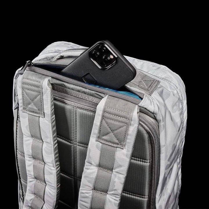 A GR1 USA - Ripstop ROBIC® rucksack by GORUCK in gray, showcasing its ultra-lightweight design with padded straps and a quilted back panel, is partially open to reveal a black smartphone nestled inside a pocket. The solid black background brings out the details of the rucksack.