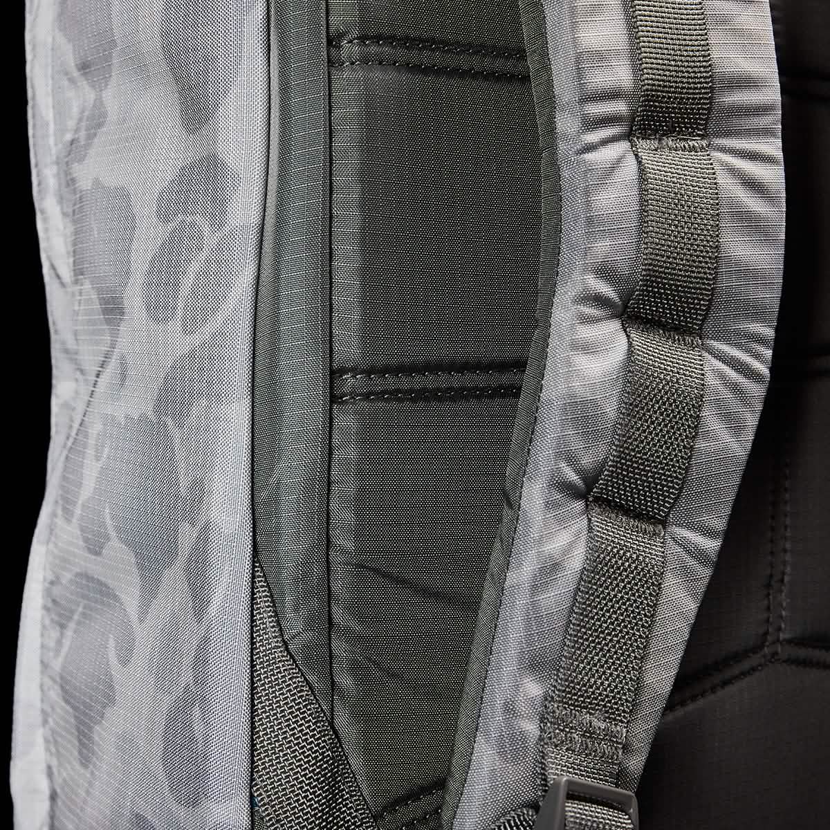 Close-up of the GORUCK GR1 USA - Ripstop ROBIC® backpack featuring a camouflage pattern. The image highlights its padded straps and detailed stitching, showcasing the texture and design of its ultra-lightweight fabric. The colors predominantly include shades of gray and green.