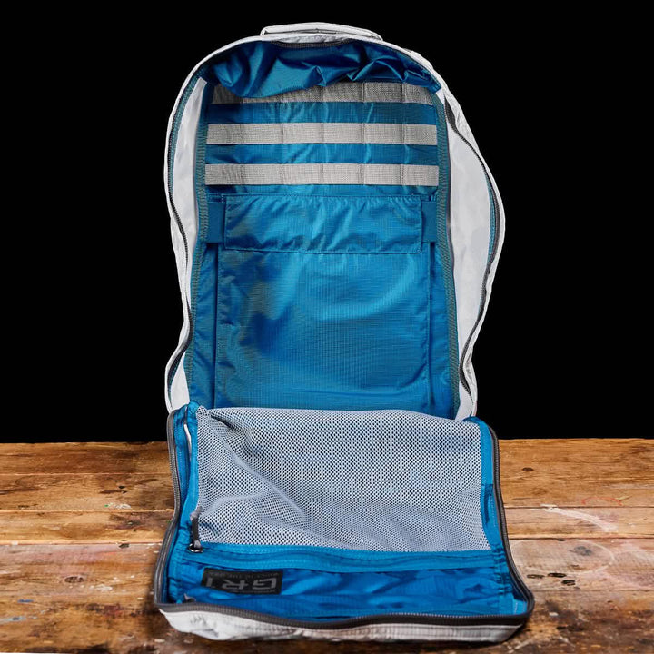 A GR1 USA - Ripstop ROBIC® backpack from GORUCK, featuring a striking blue and gray design reminiscent of an ultra-lightweight rucksack, is presented on a wooden surface. The interior includes mesh pockets and straps for organization, while the exterior remains hidden. A black background emphasizes its sleek design.