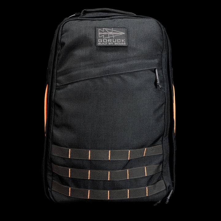 The GR1 Shooter 26L - Built by SCARS is a black backpack with orange side accents and front MOLLE webbing, crafted from Special Forces Grade CORDURA®, shown on a black background. Durable design, backed by the SCARS team guarantee.