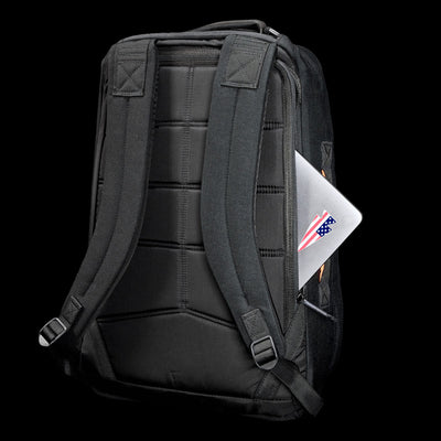 The GR1 Shooter 26L - Built by Scars backpack, crafted from Special Forces Grade CORDURA®, with visible straps, holds a laptop featuring a US flag sticker in the side pocket, all set against a black background.