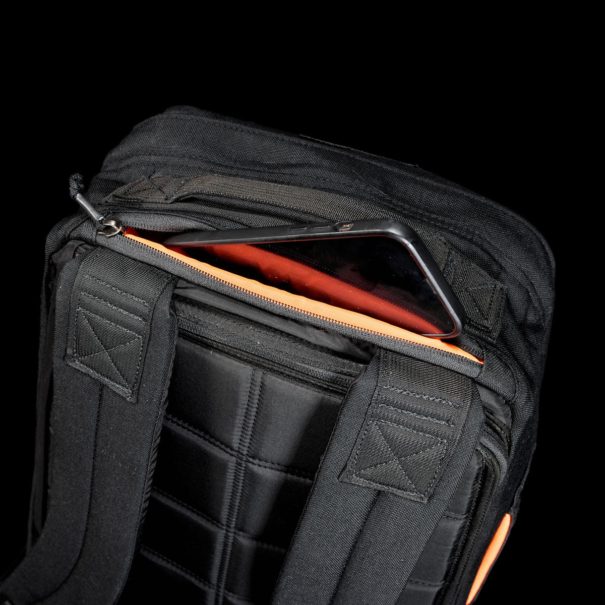 A smartphone partially tucked in a zippered pocket on a black GR1 Shooter 26L - Built by Scars backpack, crafted from Special Forces Grade CORDURA® with padded straps.