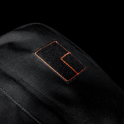 Close-up of a black Special Forces Grade CORDURA® patch with orange stitching on a black background, inspired by the legendary GR1 Shooter 26L - Built by Scars design.