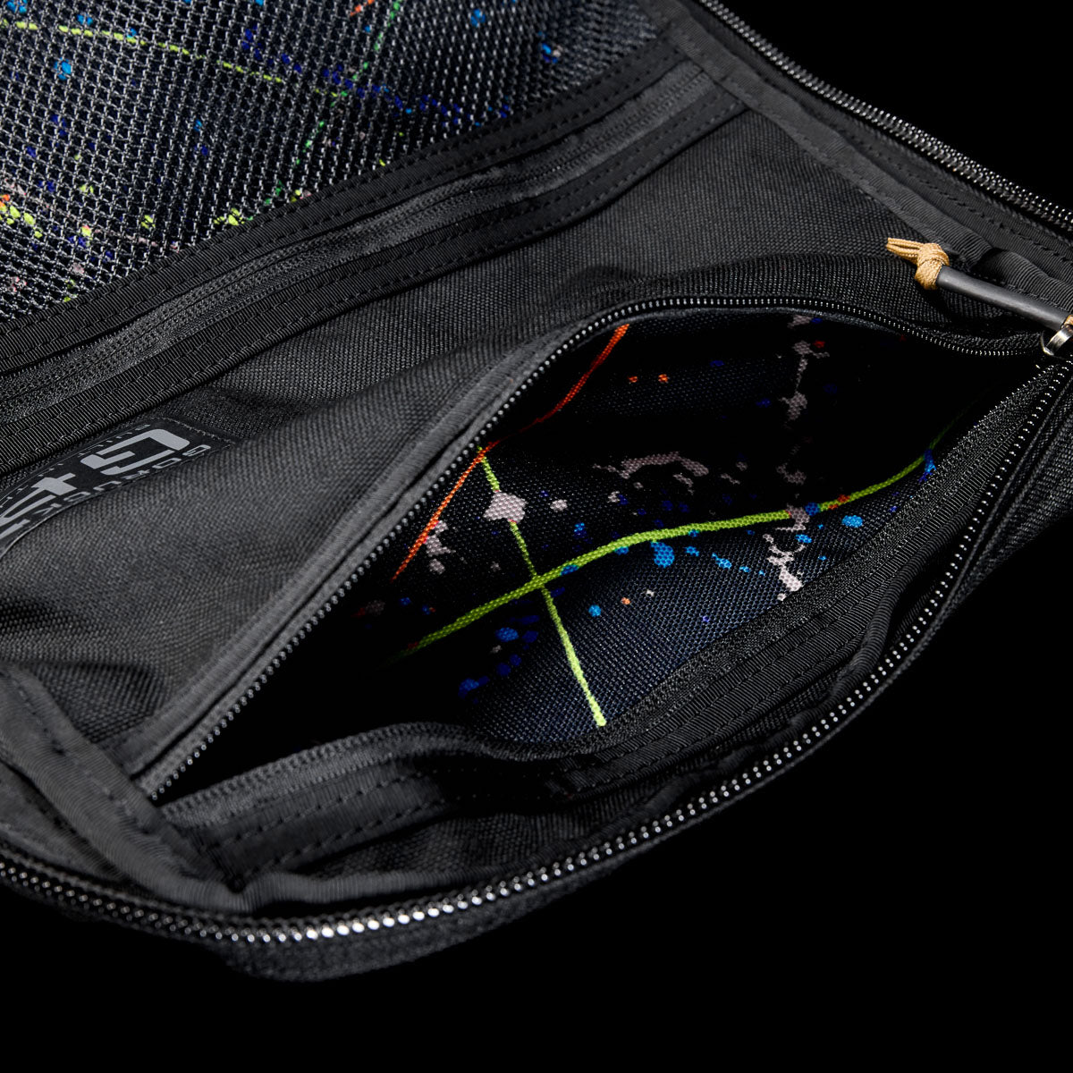 Close-up of an open black GR1 Shooter 26L pouch made from Special Forces Grade CORDURA®, revealing a colorful splatter-patterned lining. Inspired by Shooter Ruck gear and trusted by the SCARS team.