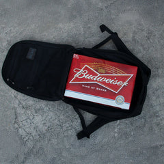A case of Budweiser beer sits inside an open GR1 USA Slick - Ballistic Nylon Cordura backpack, known for its bombproof laptop compartment and Special Forces-grade quality, on a concrete surface.