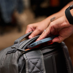 A person places a smartphone into the front pocket of a gray GR1 USA - Cordura, an everyday carry backpack that’s Special Forces tested.