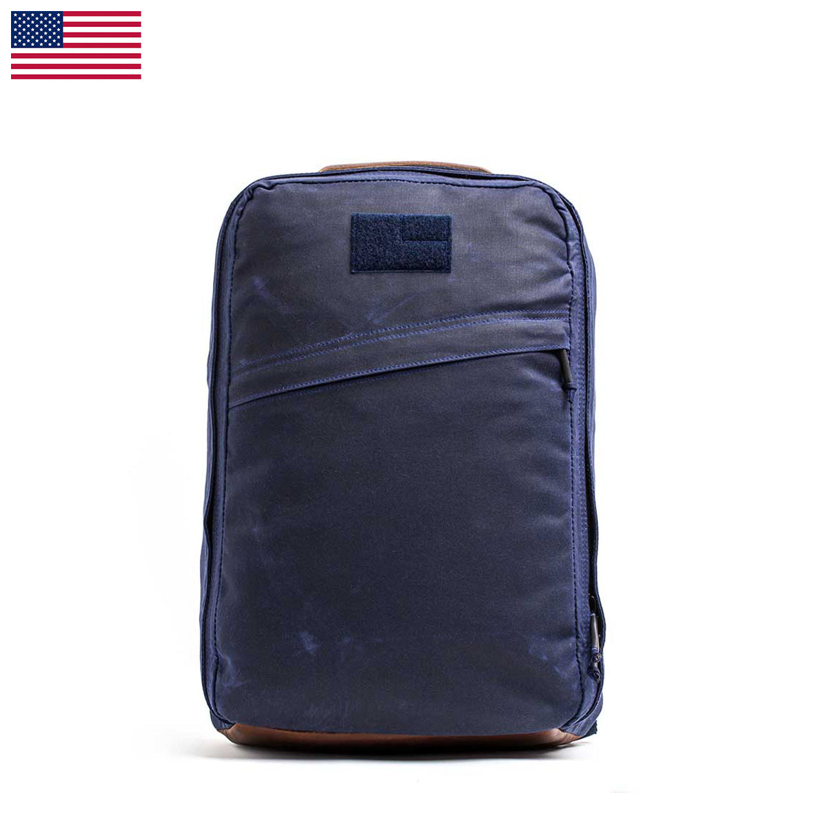 The GR1 USA - Heritage backpack in navy blue, made from waxed duck canvas with a front pocket and handle, is set against a plain white background. A USA flag graces the top left corner, adding patriotism to this functional and stylish carryall.