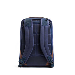 The GR1 USA - Heritage is a blue backpack with padded straps, brown accents, and a grid back panel on white. Made from durable waxed duck canvas, it includes a bombproof laptop compartment to keep your tech safe on every adventure.
