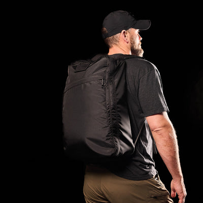 A man in a black shirt and cap carries the GR1 USA - Ripstop ROBIC® backpack, crafted from 420D Robic® Ripstop Nylon, against a dark background.