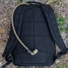 GORUCK black rucksack laid on ground with padded straps and hydration tube on outdoor terrain