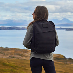 Person wearing black GORUCK rucksack outdoors with a scenic lake and mountain landscape in background