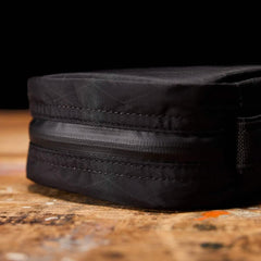 Close-up of black durable rucking pouch with zipper, placed on worn wooden surface under studio lighting
