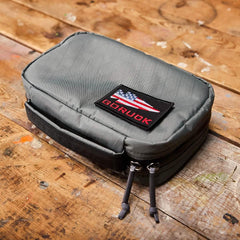 Gray GORUCK compact gear pouch with American flag patch on worn wooden surface