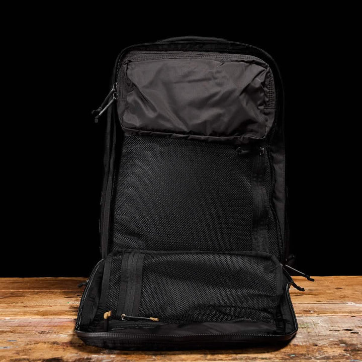 Set against a wooden surface with a black background, the open GR2 - Ripstop ROBIC® by GORUCK is a versatile travel bag made from water-resistant materials. The interior is designed for organized storage with multiple compartments and mesh pockets, making it an ideal rucksack for all your adventures.