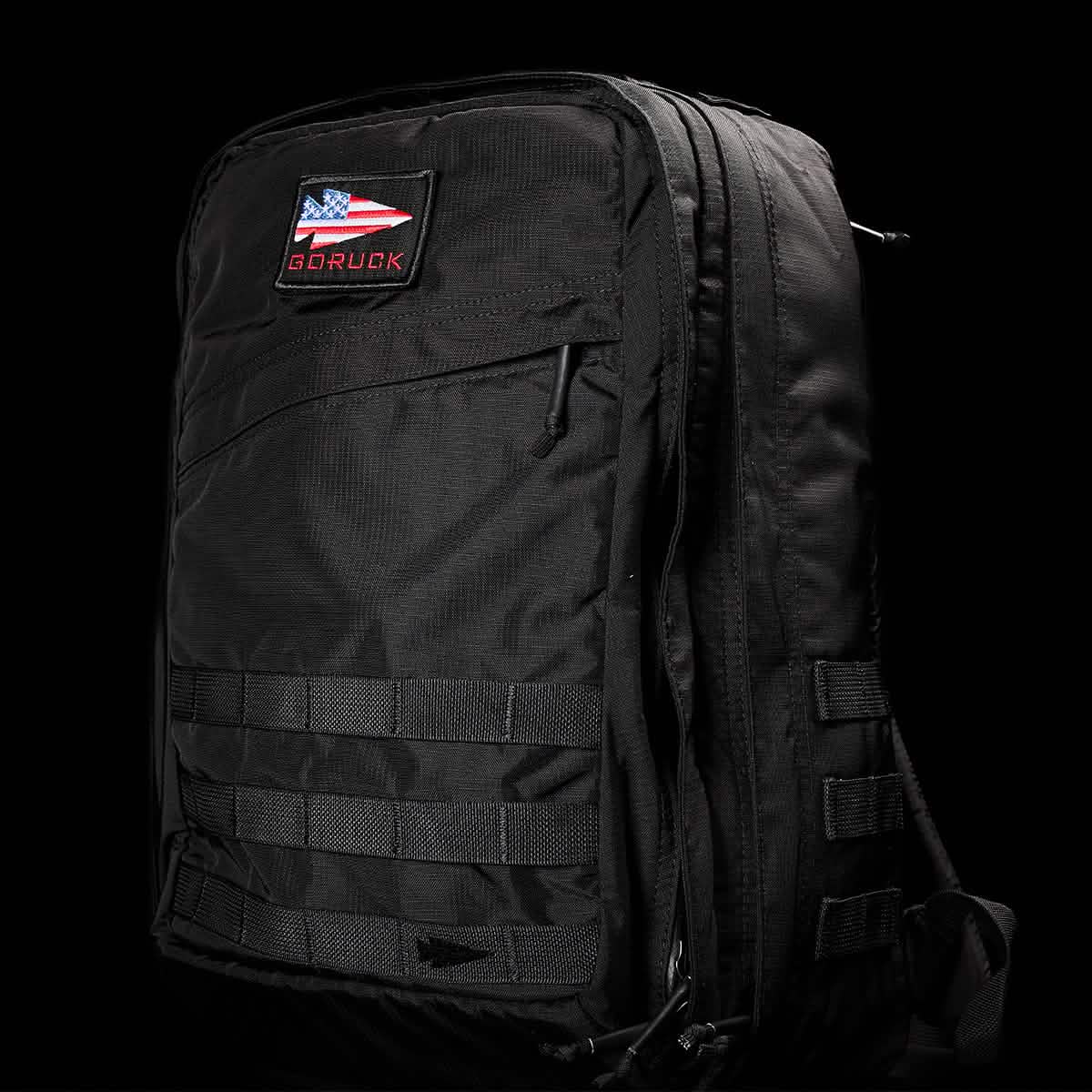 A GR2 - Ripstop ROBIC® by GORUCK in black, featuring multiple compartments and a patch with an American flag and the text GORUCK on the front. The dark background accentuates its sleek, water-resistant design and rugged texture, making it ideal for any adventure.