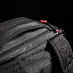 A close-up of a black zippered bag, echoing the robust design of the GORUCK GR2 - Cordura used by Special Forces, highlights vibrant red pull tabs set against a dark backdrop. The material looks durable, with clearly visible stitching and seams.