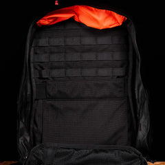 The GR2 by GORUCK, a black ruck designed for Special Forces use, is set against a matching background and features an eye-catching orange interior lining. It resembles a travel bag with multiple storage compartments, including mesh pockets and webbing for optimal organization.