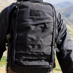 Close-up of a black GORUCK rucksack worn on a person hiking in mountainous terrain