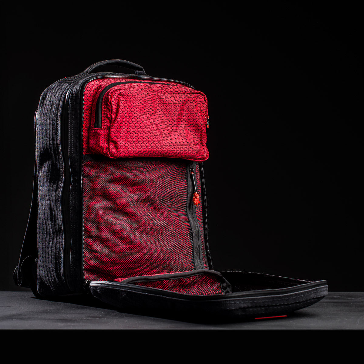 The GR2 x Carryology - GRXC2 Samurai 2.0, a black JPXDP denim backpack with a red mesh-lined front pocket, sits unzipped and open against a black background.