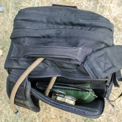 Top view of a black GORUCK rucksack with a partially open zipper showing green and beige gear inside on dry grass