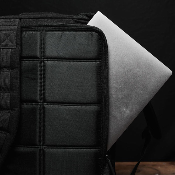 A silver laptop partially tucked into a black padded backpack against a dark background.