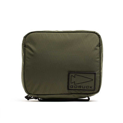 The GR2 Field Pocket - X-PAC is an olive green electronics organizer pouch with a black arrowhead logo patch on the front, made from waterproof fabric and shown against a white background.