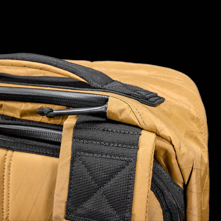 Close-up of the GR2 X-PAC tan backpack featuring black X-PAC fabric and AquaGuard zippers for waterproof protection, set against a solid black background.