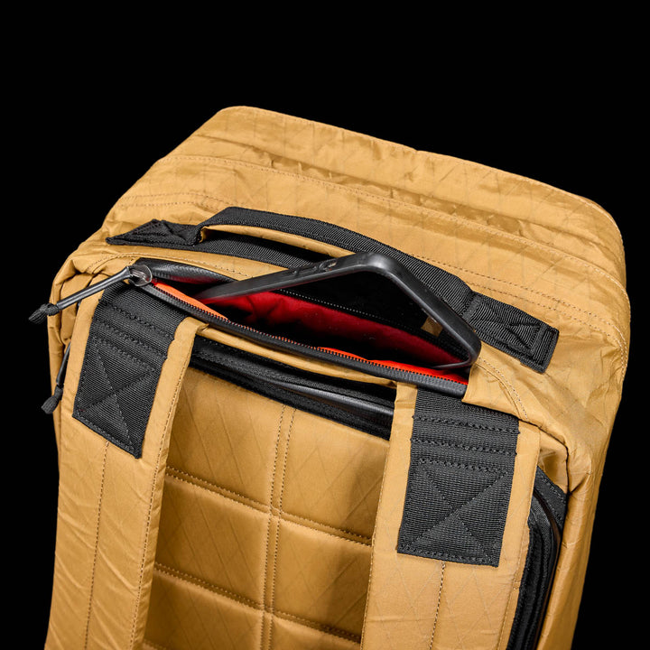The GR2 X-PAC backpack in tan with black straps is partially unzipped to show a tablet in its red-lined compartment and features AquaGuard zippers for enhanced waterproof protection.