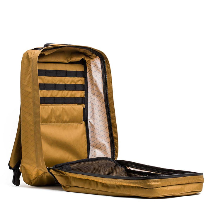 The GR2 X-PAC tan backpack with AquaGuard zippers is open, showing interior pockets and a mesh divider inside its main waterproof compartment.