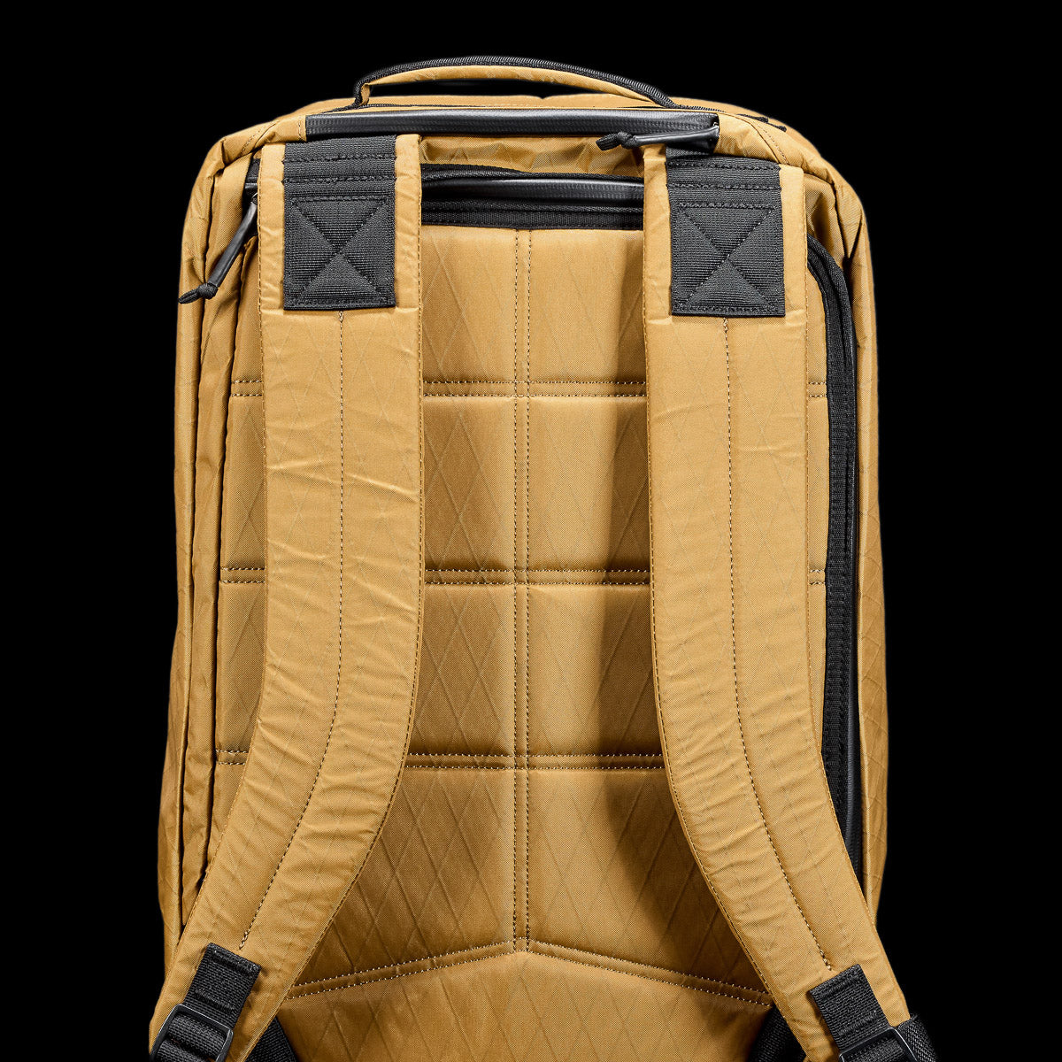 A tan backpack with quilted padding and black accents on the shoulder straps, shown from the back.
