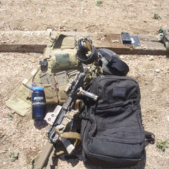 GORUCK GR2 black backpack with tactical gear including rifle, body armor, headset, and water bottle on gravel