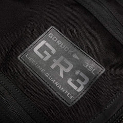 Close-up of a black fabric patch on a carry-on rucksack displaying the text: GORUCK - GR3® - Cordura LIFETIME GUARANTEE. The rugged, water-resistant patch is stitched onto the fabric, highlighting durability and quality.