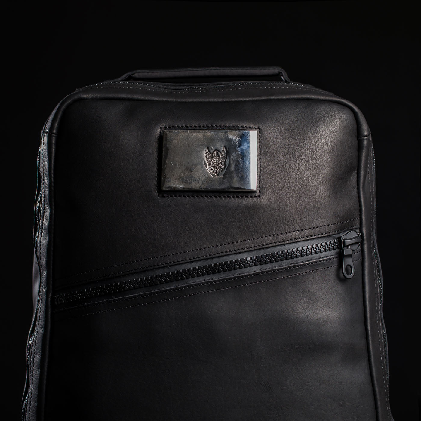 The GR1 USA x Carryology - Berserker Viking is a black leather backpack with a diagonal zipper and a metallic heart emblem patch, inspired by the resilience of Viking warriors.