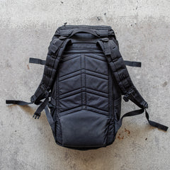 Black GR MONSTER Rucksack - PREORDER with padded straps, viewed from the back and resting on a rough, light-colored concrete surface—a classic style by GORUCK.