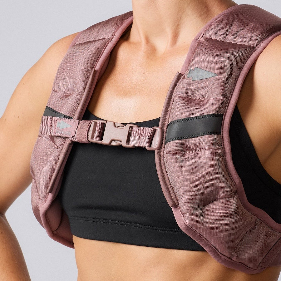 Person wearing a pink weighted vest over a black sports bra, shown from the shoulders to the torso.