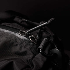 Close-up of a GORUCK Gym Bag - Ripstop ROBIC® backpack highlights the zipper and pull tags. The textured ripstop nylon with detailed stitching features metal zippers and loops. The dark background emphasizes the bags design, suggesting a concealed shoe compartment for extra convenience.