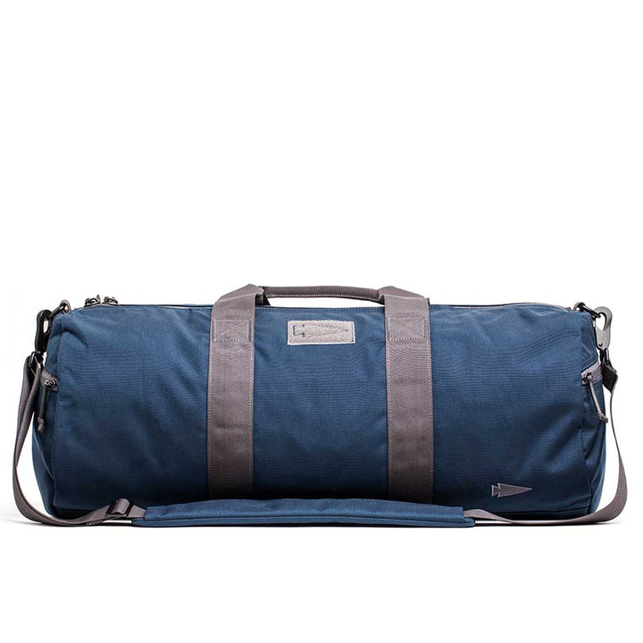 The Gym Bag - Cordura is a blue duffel with gray straps, a side pocket, and crafted from durable CORDURA material. Its sleek design on a white background suits fitness enthusiasts perfectly. It also includes a lifetime guarantee for peace of mind.