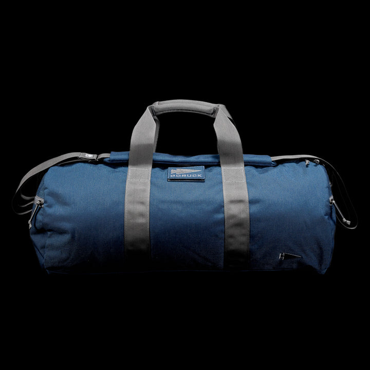 The Gym Bag - Cordura is a blue duffel crafted from durable CORDURA, featuring gray handles and a shoulder strap on a black background.
