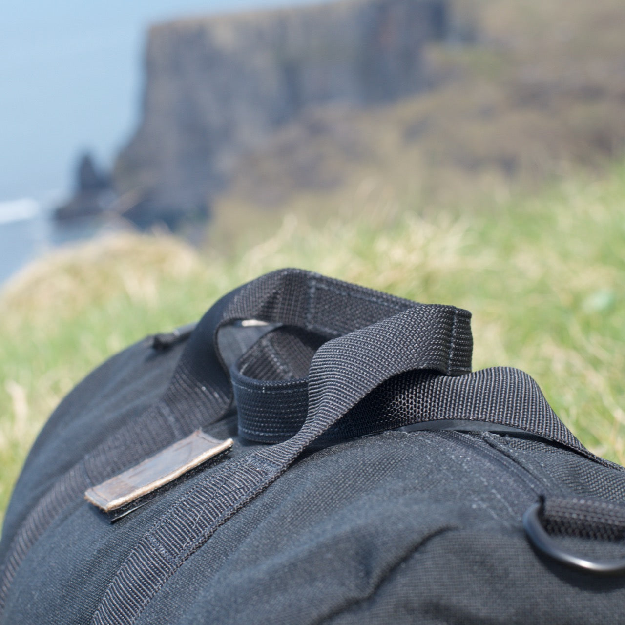 Close-up of the Gym Bag - Cordura, made from durable 1000D CORDURA fabric, resting on grass with blurred cliffs and ocean in the background.