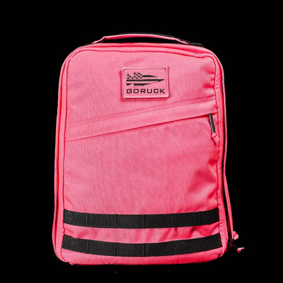 A vibrant pink GORUCK GR0 - Cordura backpack, featuring black horizontal straps on the front and a patch showcasing the brand logo, is designed as a compact option. It includes a bombproof laptop compartment, ideal for minimalist EDC needs, set against a solid black background.