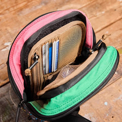 An open Admin Panels wallet from GORUCK, placed on a wooden surface, exhibits an array of credit cards and compartments. This vibrant accessory, featuring pink and green fabric, is perfect for everyday carry (EDC). Its zip closure ensures everything stays secure, making it ideal for travel adventures.