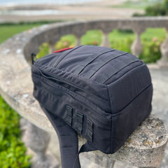 A black GR2 ruck, ideal for one bag travel, sits on a stone railing against a blurred outdoor backdrop.