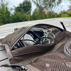A Wire Dopp - Waxed Canvas organizer filled with tangled cables and a mouse rests on a wooden outdoor table.