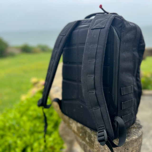 A GR2 backpack rests on a stone ledge outdoors, ideal for one bag travel, with greenery and water softly blurred in the background.