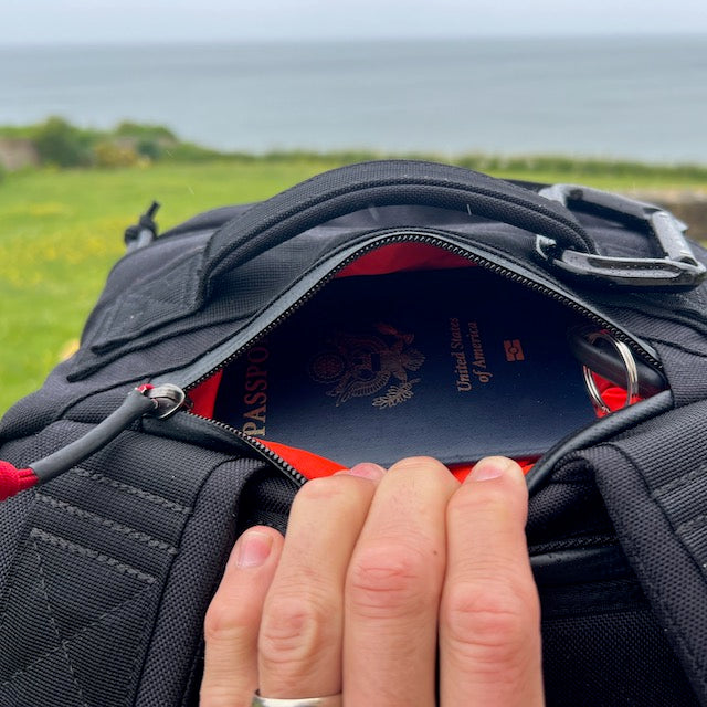 A hand opens the GR2 backpack, revealing a U.S. passport inside with an ocean view in the background—ideal for one-bag travel and carry-on adventures.