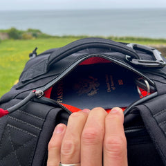 A hand opens the GR2 backpack, revealing a U.S. passport inside with an ocean view in the background—ideal for one-bag travel and carry-on adventures.