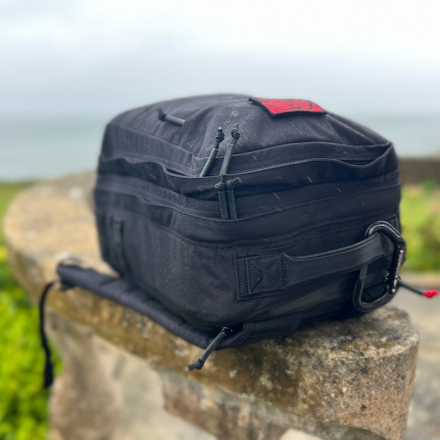 A GR2 backpack rests on a stone ledge outdoors, ideal for one bag travel, with the ocean in the background.
