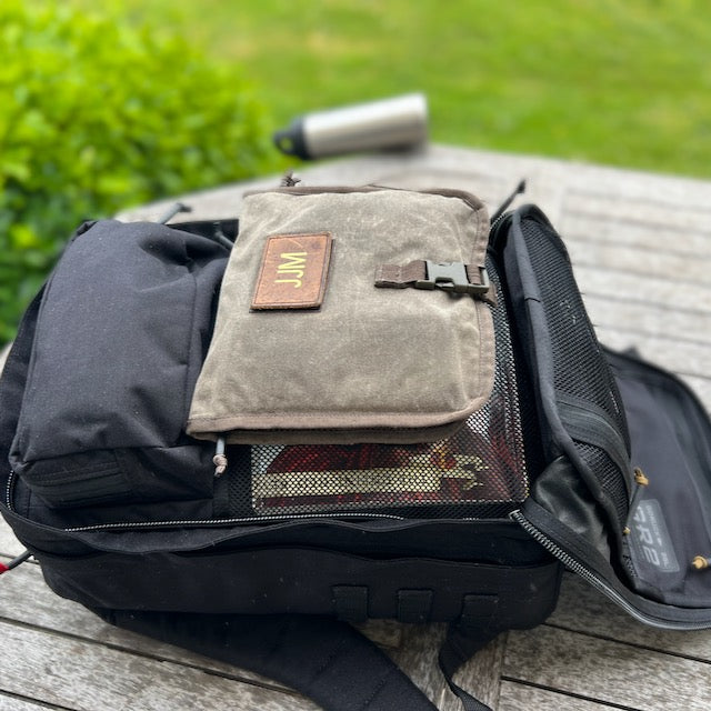 A black GR2 backpack rests on a wooden outdoor table, with a water bottle behind it—ideal for one bag travel and carry-on use.