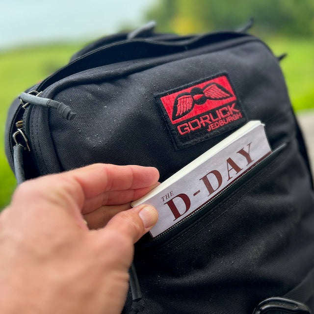A hand places a book into the GR2 outdoors, highlighting the simplicity of one bag travel with this carry-on compliant GORUCK backpack.